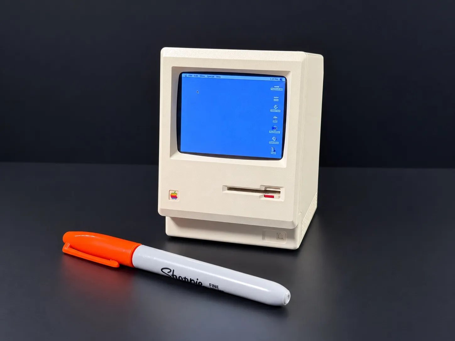 The Macintosh Mini switched on at the Mac desktop, a Sharpie in front of it for scale